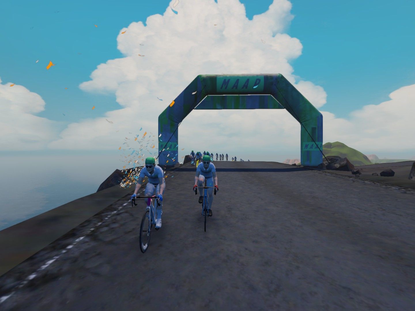 A group of cyclists dressed in light blue uniforms rides toward a large green and blue archway labeled 