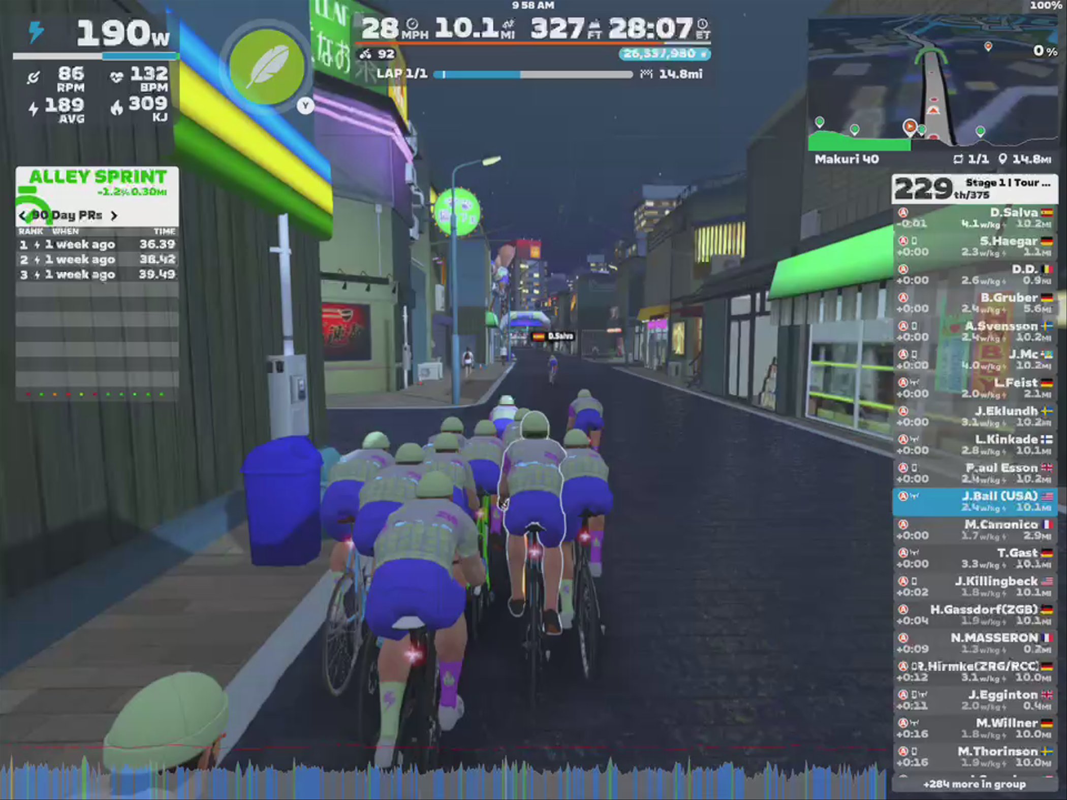 A virtual cycling scene in Zwift features a group of cyclists riding together on a dimly lit street. The environment includes colorful neon signs and buildings, with various statistics displayed on the screen, such as power output and lap times. The cyclists are in a close formation, navigating the virtual landscape.