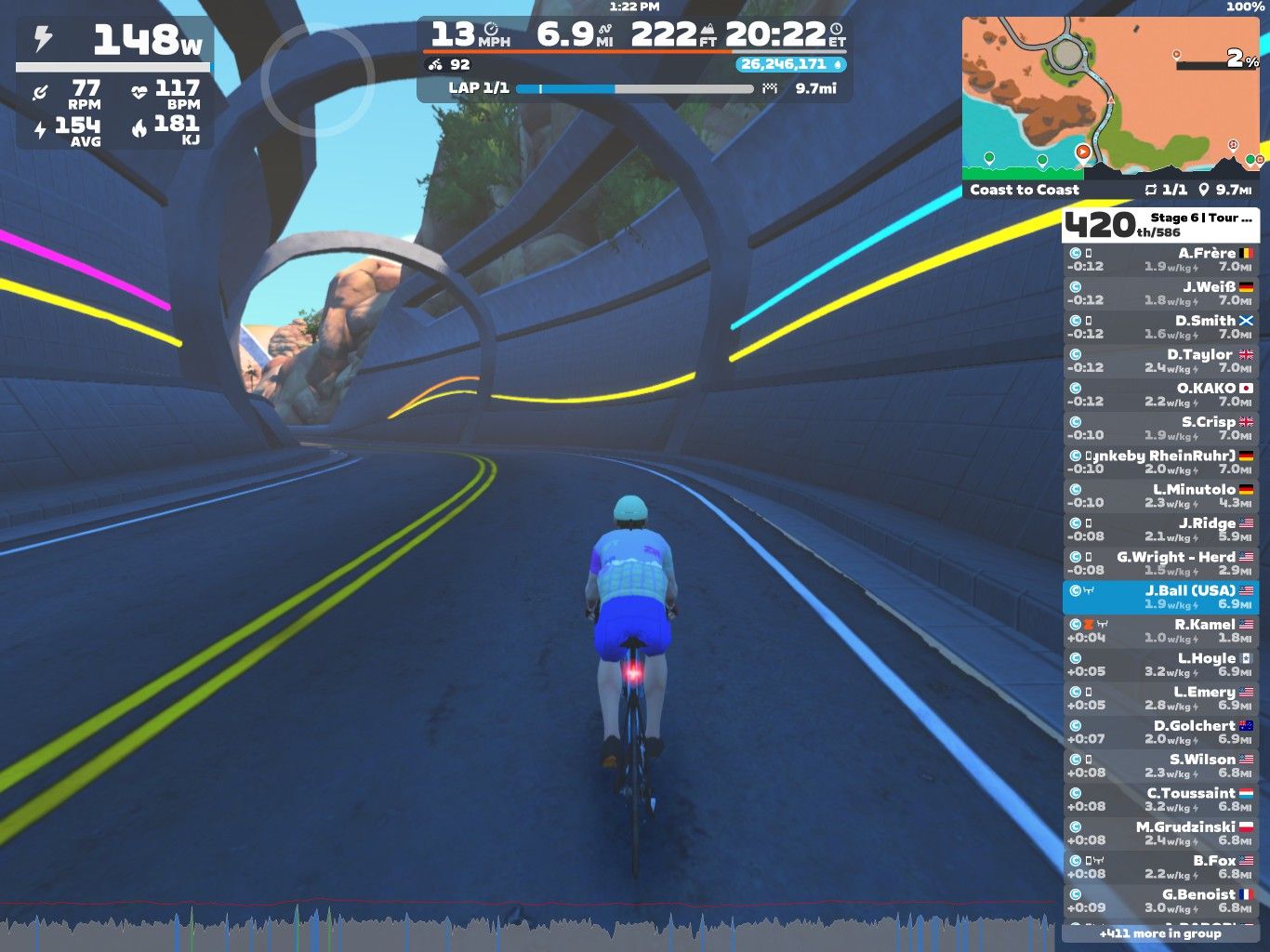 A cyclist is riding through a virtual tunnel in a gaming application, Zwift. The rider is wearing a light blue and white outfit and is surrounded by colorful lines on the tunnel walls. The display shows various performance statistics, including power output, speed, and distance. A map and leaderboard are visible on the right side of the screen. The scene captures a dynamic and immersive cycling experience in a digital environment.