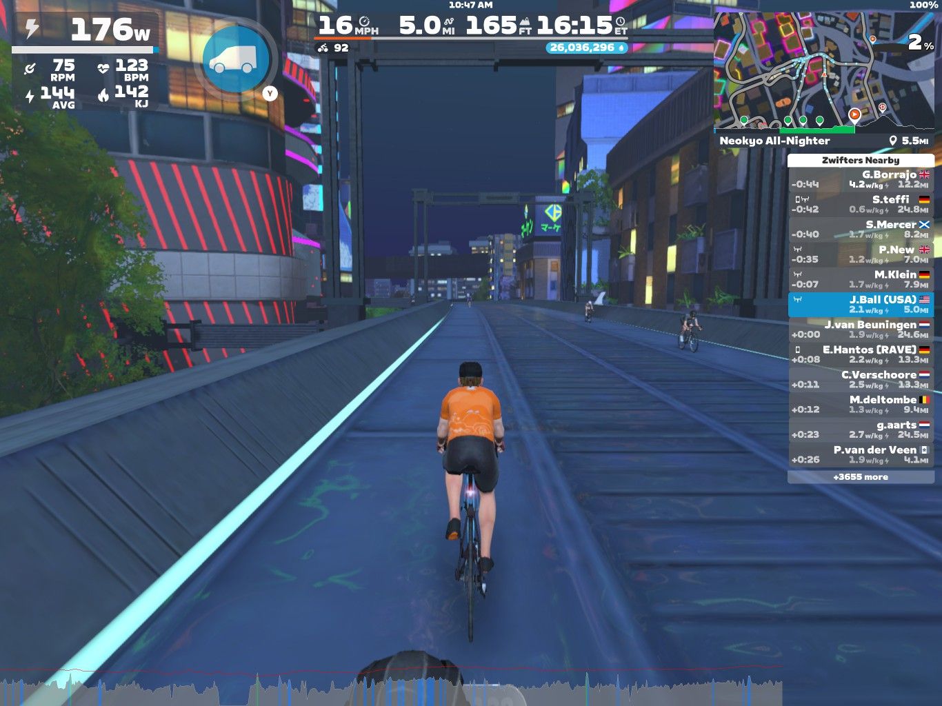 A cyclist in an orange shirt rides on a virtual road in Zwift, surrounded by neon-lit buildings at night. The screen displays various performance metrics, including power output, speed, and heart rate, along with a list of other cyclists nearby. A map of the virtual location is shown in the upper right corner.
