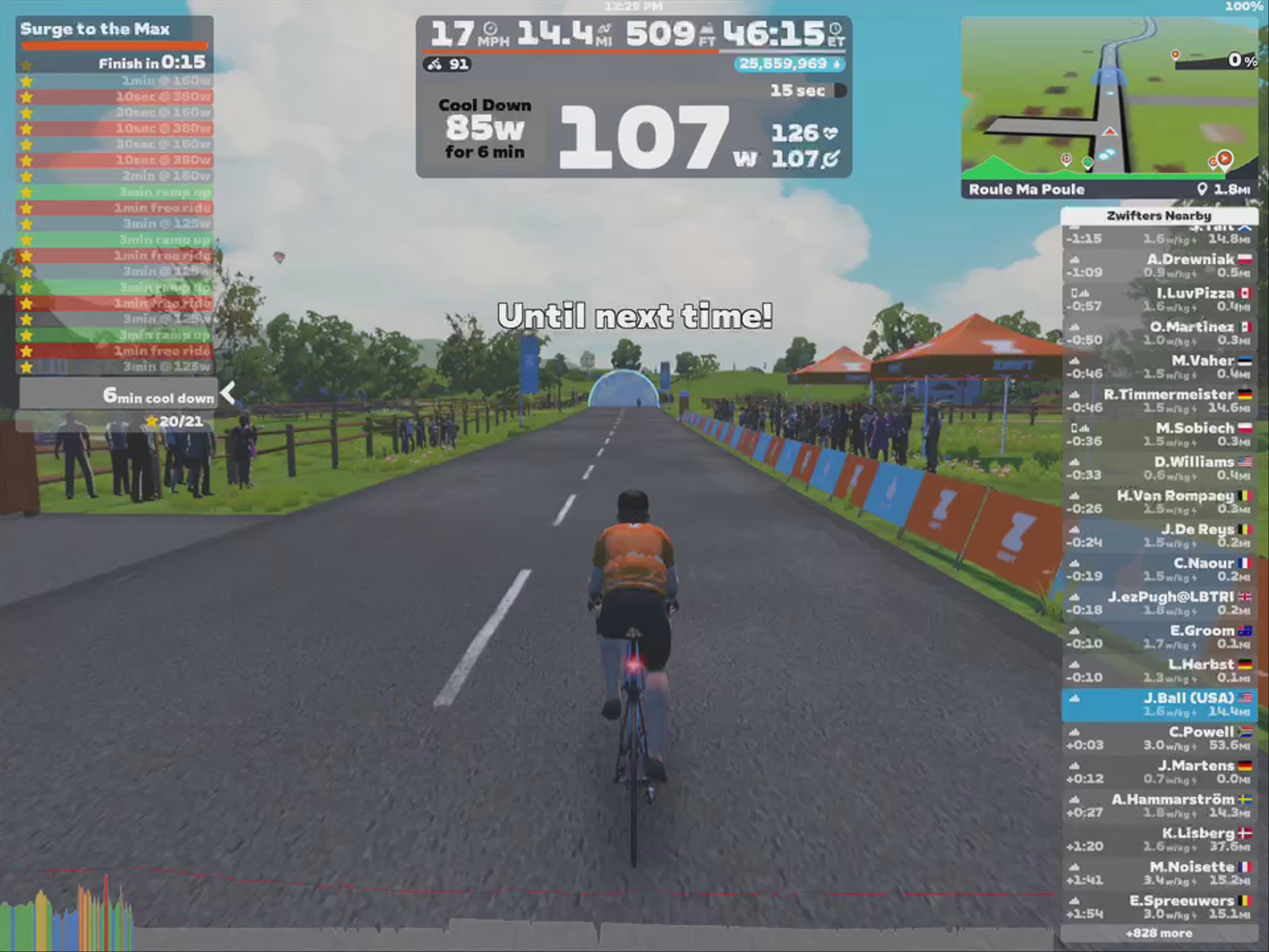 A cyclist in an orange shirt rides along a virtual road in Zwift, with a timer displaying 15 seconds until completion of a cooldown phase. On the left side, a list outlines workout details and achievements. In the background, there are spectators and a digital map showing nearby Zwifters and routes. The scene is bright and colorful, reflecting a dynamic cycling environment.