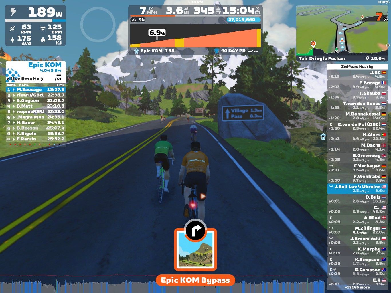 Three virtual cyclists ride on a winding road in a scenic mountainous landscape. The interface displays performance metrics, including power output and heart rate. A leaderboard shows ranks and times for the 