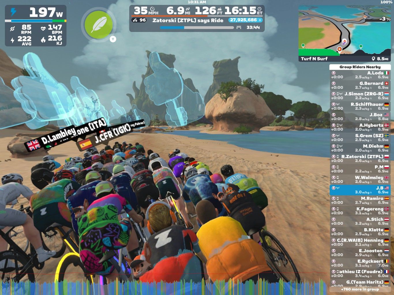 A group of cyclists participating in a virtual ride on Zwift, riding along a scenic beach pathway. The image displays various cycling statistics, including power output, cadence, and heart rate. Several colorful jerseys are visible on the riders, and digital thumbs-up icons are shown in the background. The map indicates the location 