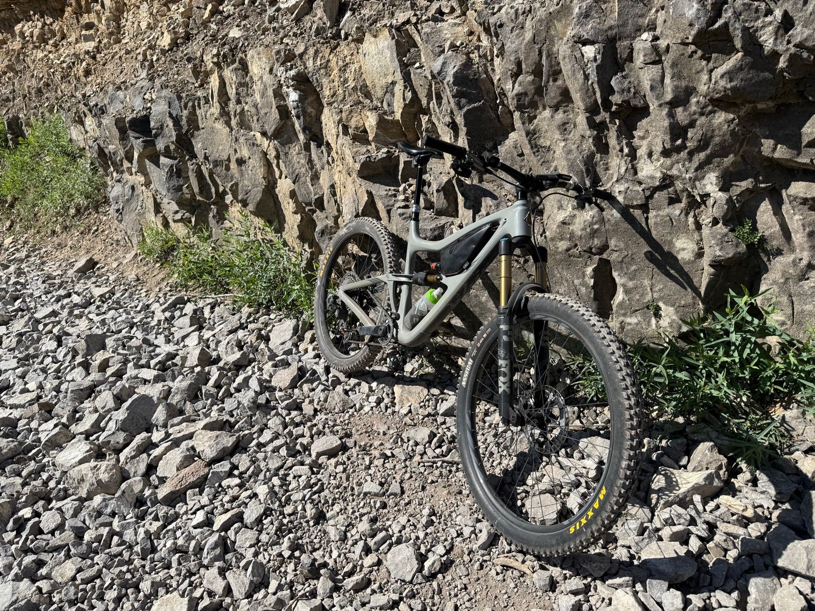 A mountain bike is resting on a rocky trail beside a steep rock wall in Providence Canyon, Utah. Green plants are visible along the path.
