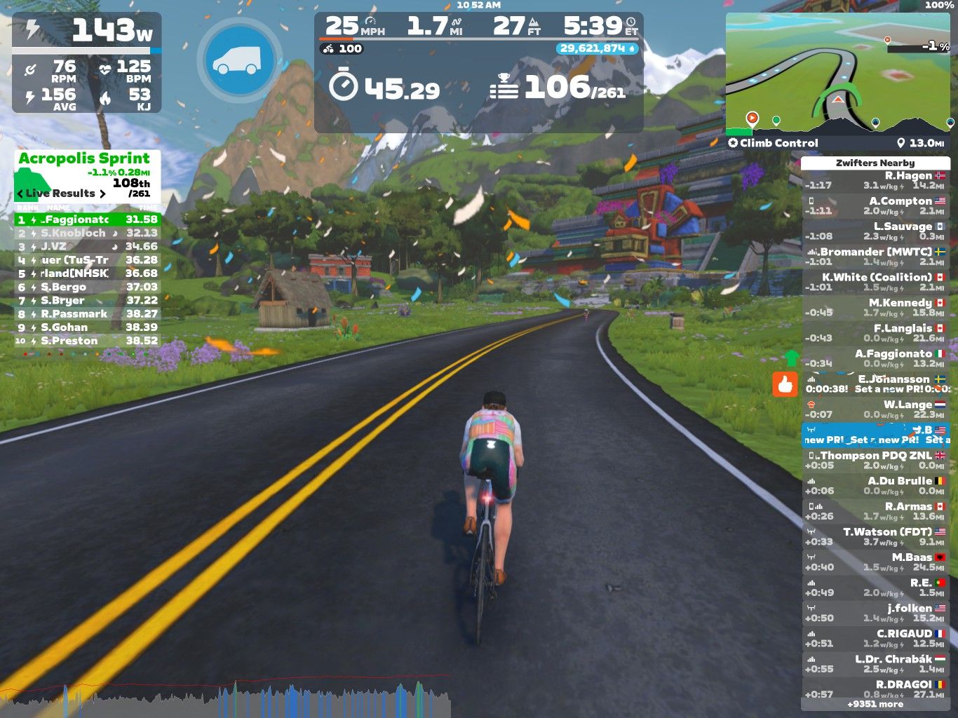 A cyclist is riding on a virtual road in Zwift, with a vibrant landscape featuring mountains, trees, and houses in the background. The screen displays various performance metrics, such as power output, speed, distance, and heart rate, along with live race results and nearby competitors. The scene is colorful and dynamic, showing a mix of technology and nature.