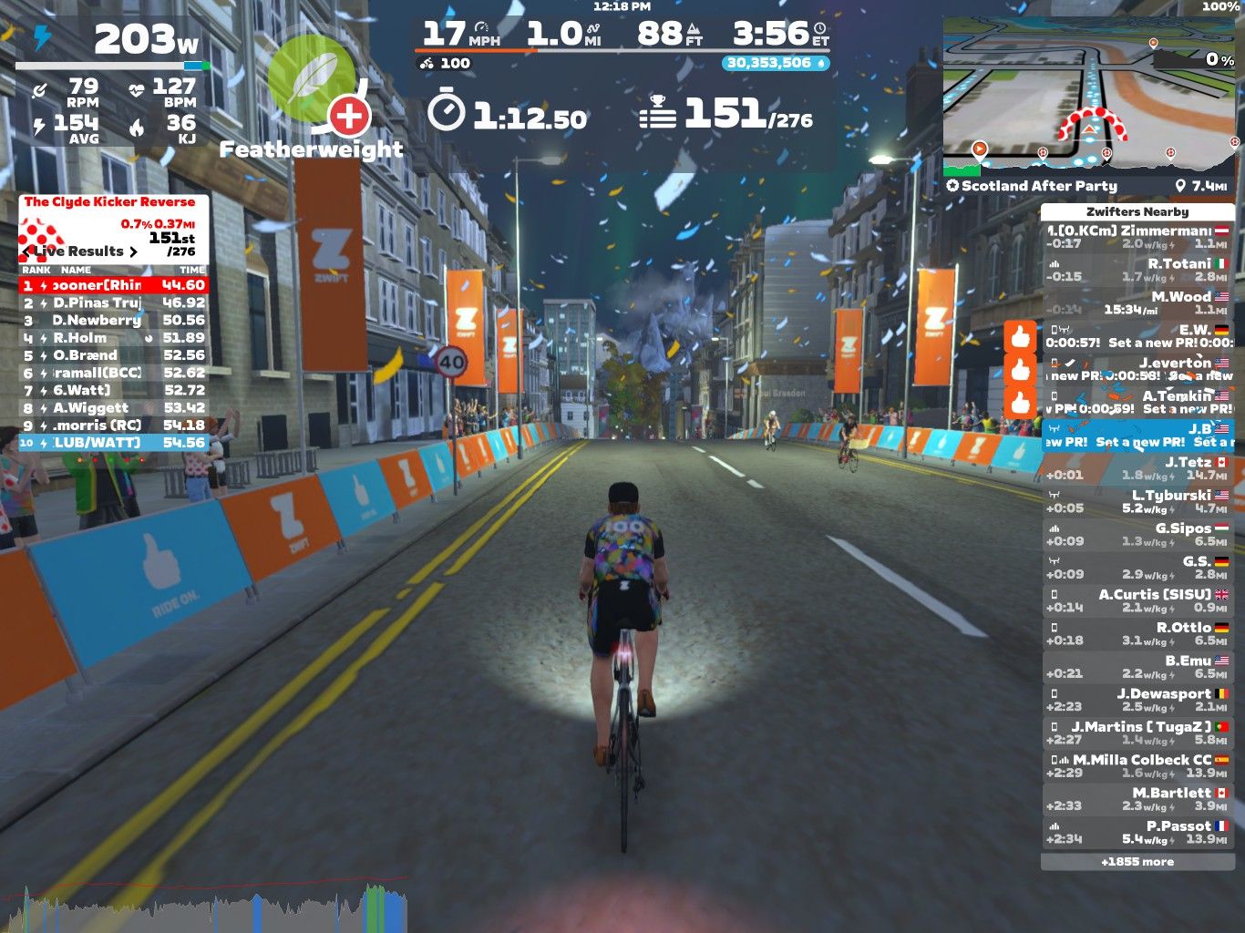 A cyclist rides down a digital street in the Zwift virtual cycling platform. The scene shows a city environment with buildings and colorful banners. On-screen statistics include power output, speed, cadence, heart rate, and rankings for participants in a cycling event. Snowflakes are falling in the virtual scene, and additional metrics about nearby cyclists are displayed.