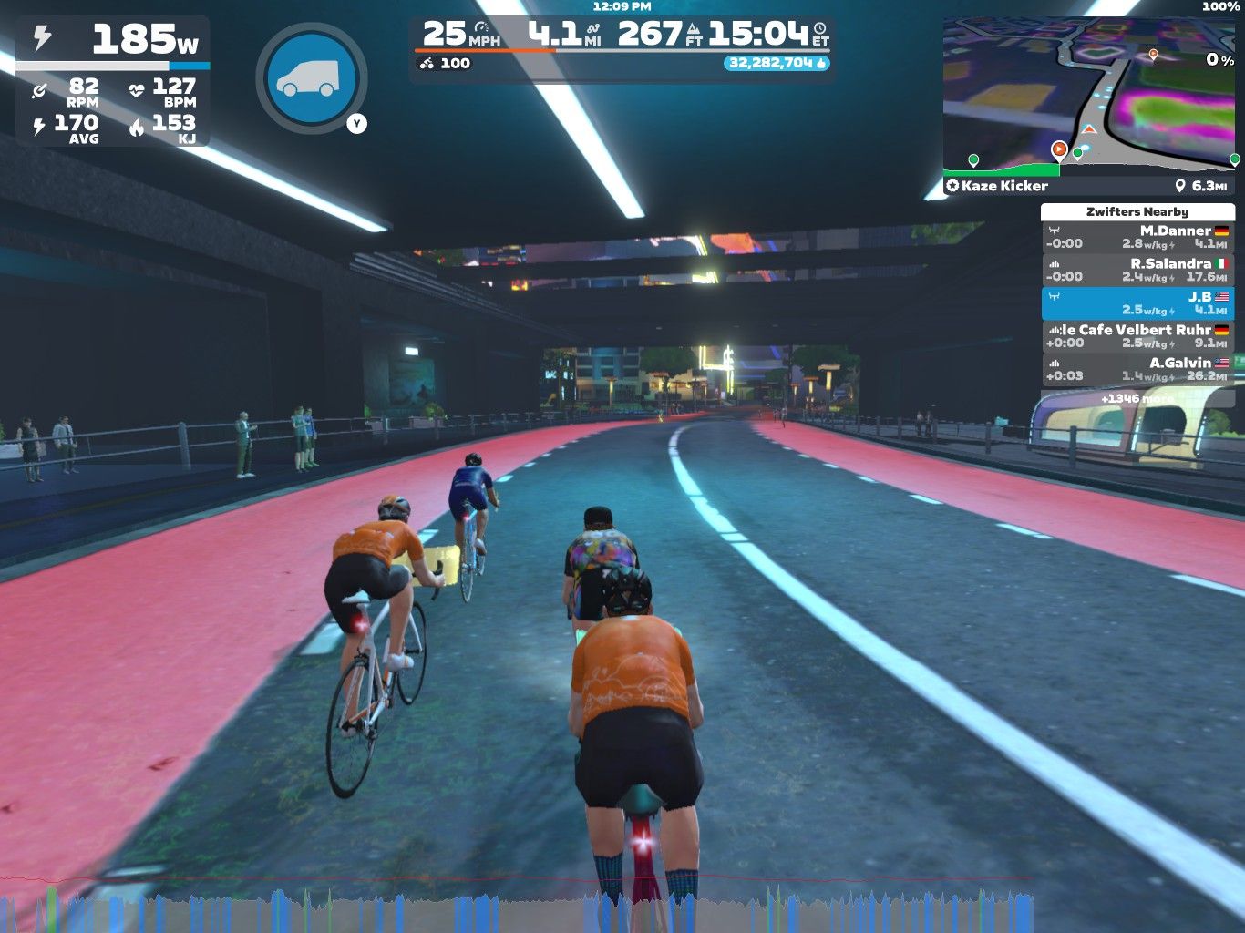 Alt text: A virtual cycling scene in Zwift showing four cyclists riding on a digital road. The background features a futuristic cityscape with spectators on the sidelines. There is a user interface displaying speed, power, and other cycling metrics.