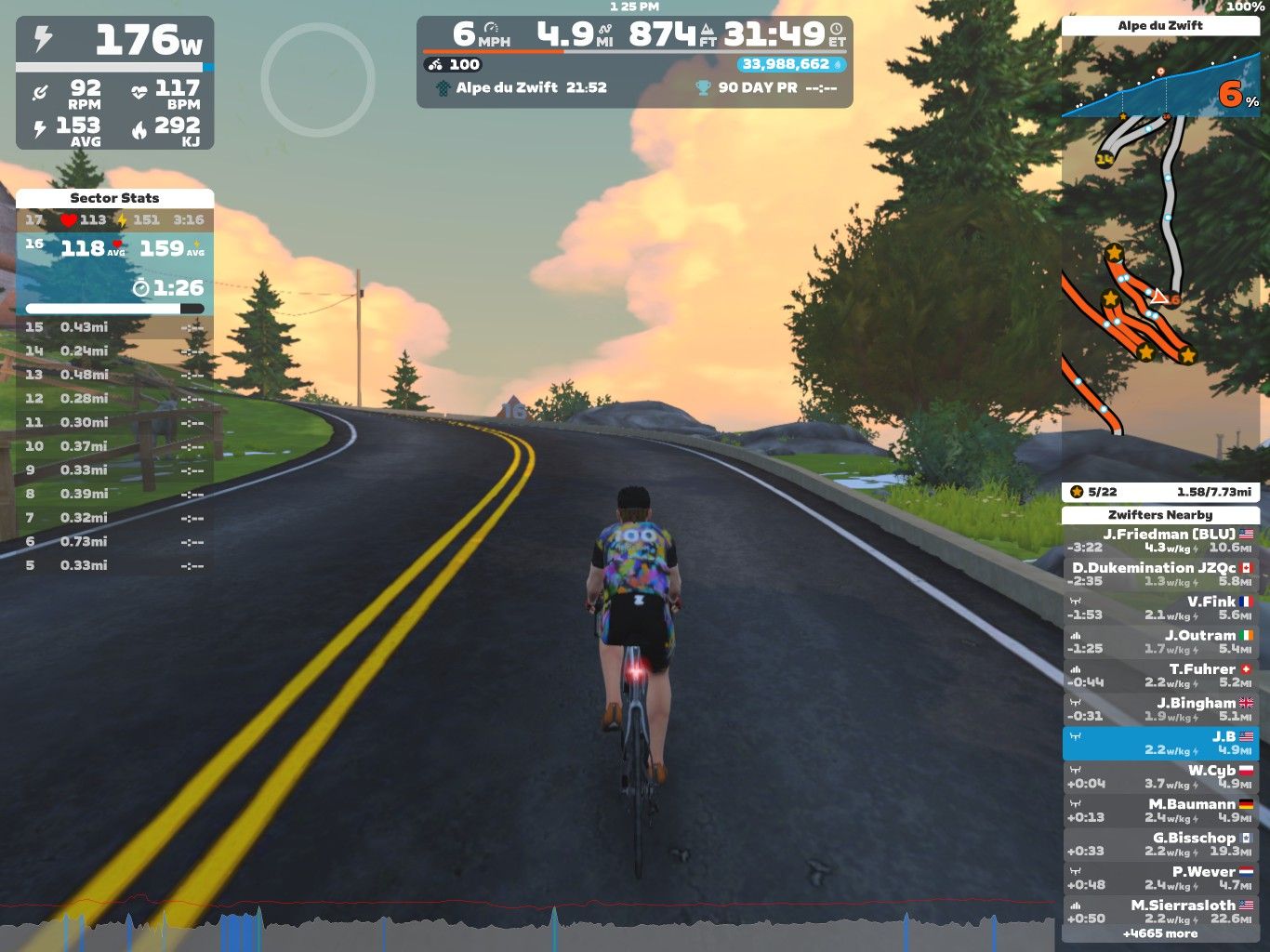 A cyclist is riding on a virtual road in Zwift, surrounded by trees and a colorful sky. The cyclist's avatar is wearing a colorful jersey, and the screen displays various statistics, including speed, distance, elevation, and heart rate. Roads curve ahead, leading up to a hilly terrain.