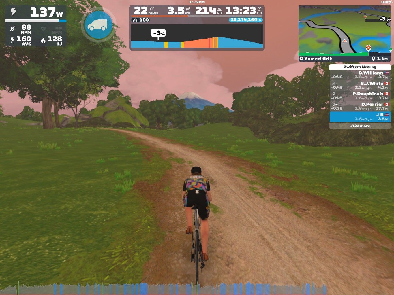 A cyclist rides on a dirt path in a virtual landscape, surrounded by trees and rolling hills. The display shows various cycling statistics, including speed, distance, and power output. The sky has a pinkish hue, indicating a dynamic environment in the Zwift platform.