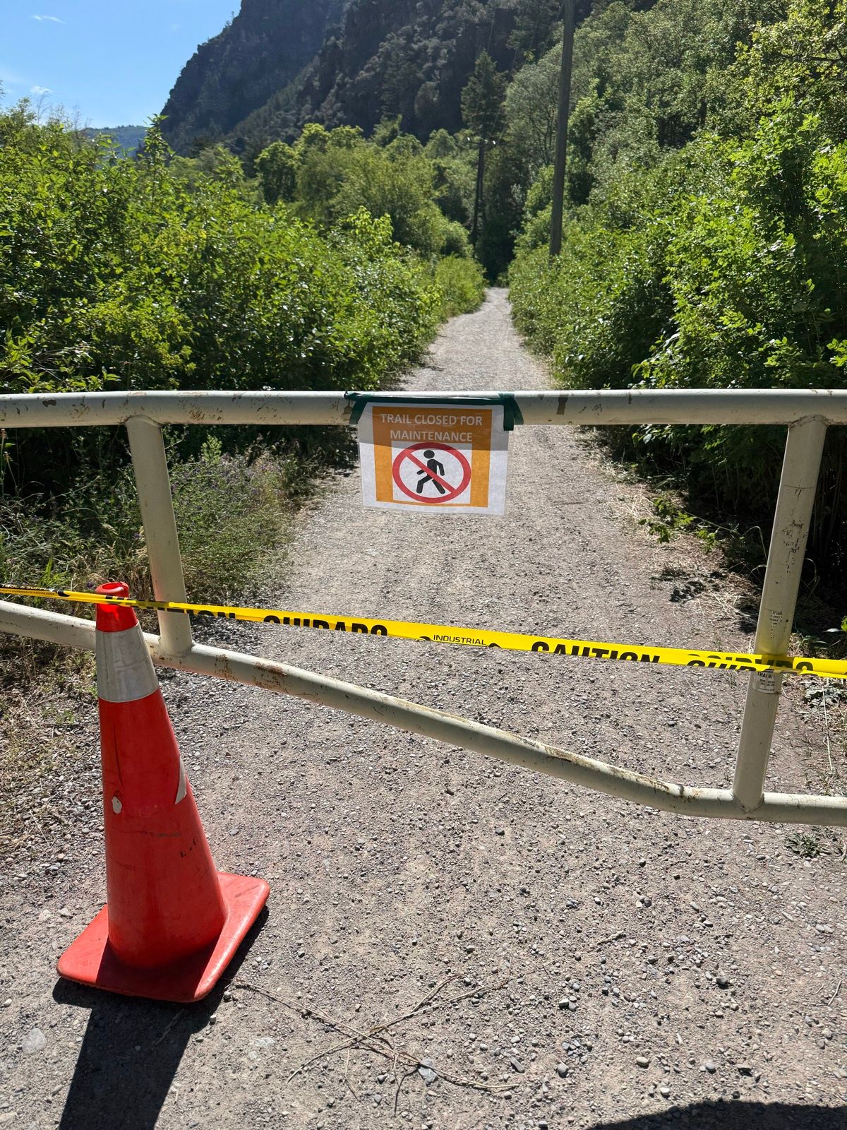 A gravel trail is closed off by a white gate with a sign that reads 