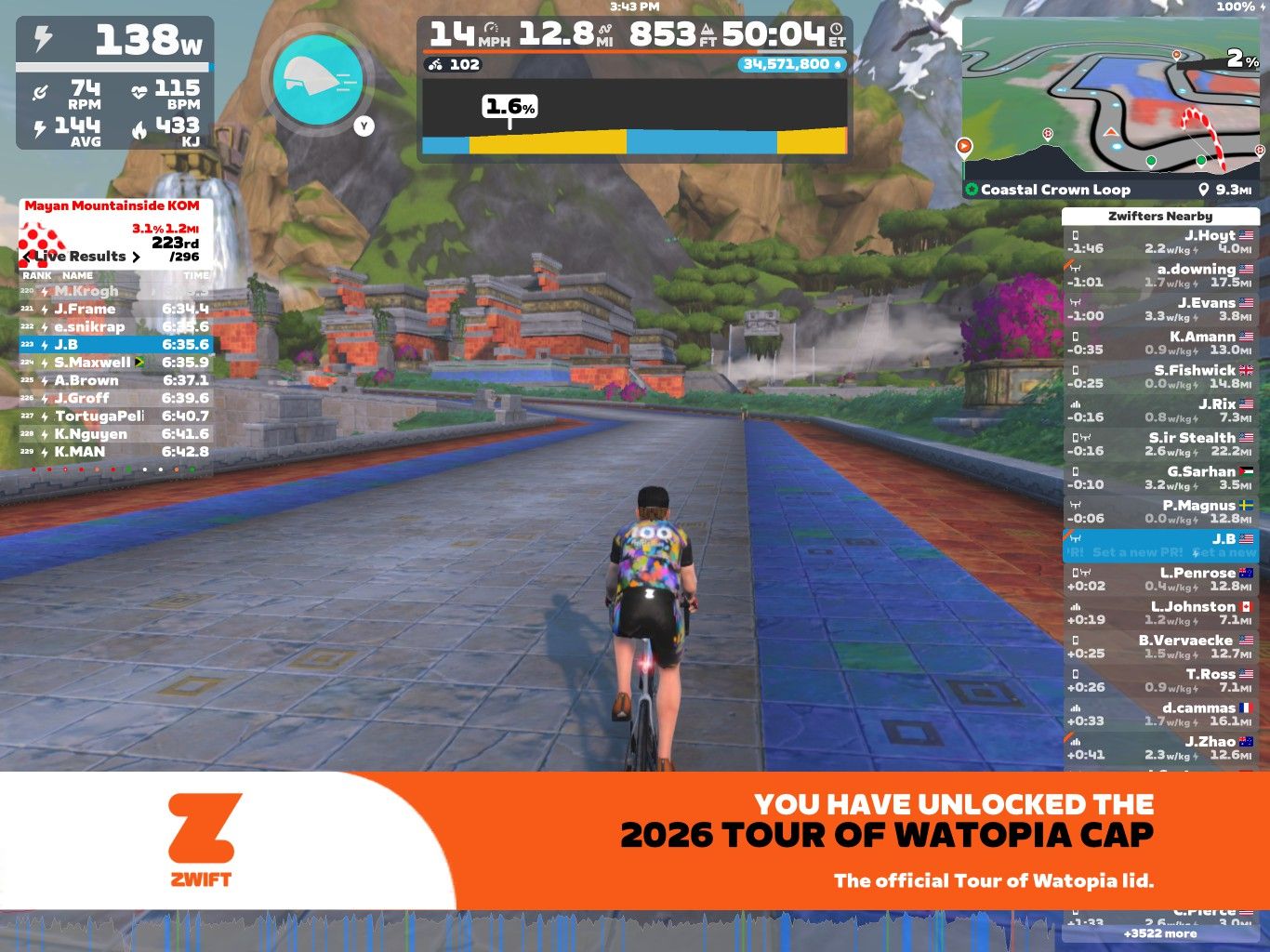 A cyclist riding in a virtual environment on Zwift, with a colorful road and scenic mountain backdrop. The screen displays performance metrics, including speed, power, and elevation, along with a leaderboard and a notification about unlocking a virtual cap for the 2026 Tour of Watopia.